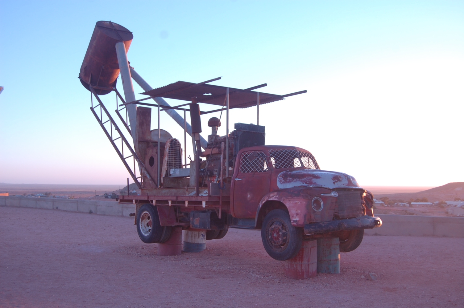 One of Coober Pedy's iconic mining vehicle is lit by the light of the rising desert sun.